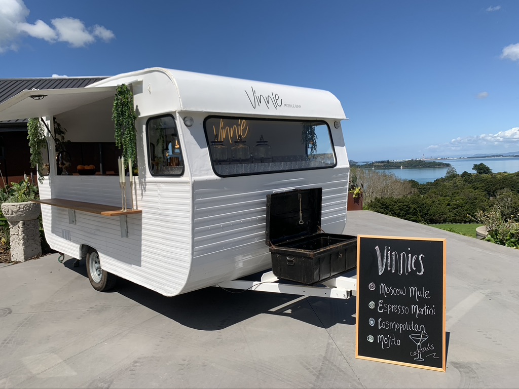 Vinnie parked with a hand-lettered cocktail menu chalkboard and ocean view