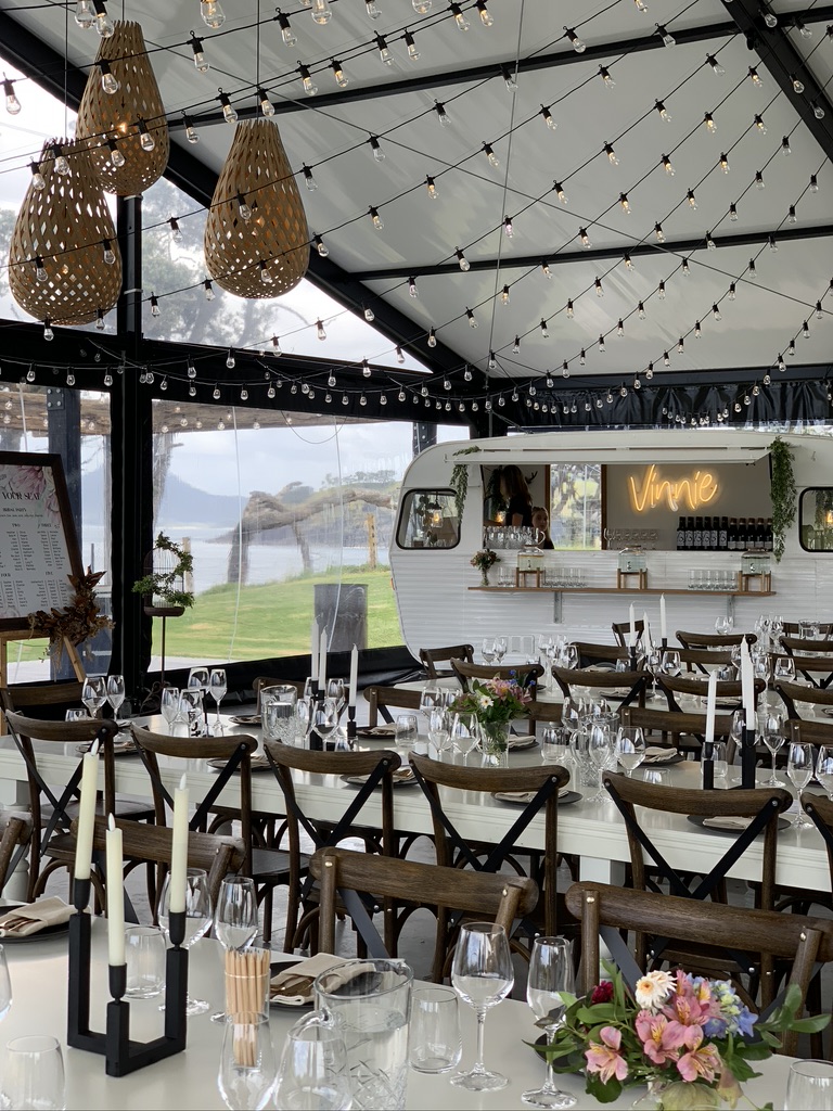 Long dining table set for a wedding with Vinnie the caravan bar glowing in the background